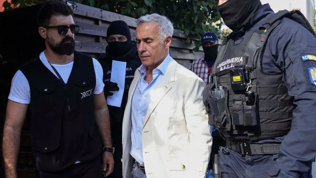 Călin Georgescu, în sacou deschis la culoare, alături de un agent cu vestă DIICOT și jandarmi mascați.