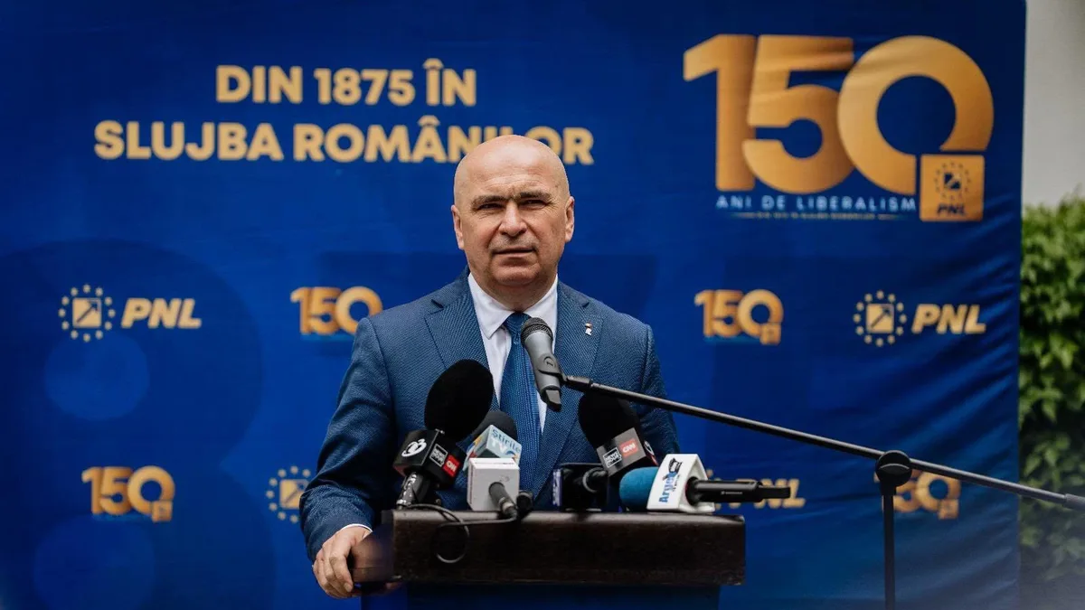 Ilie Bolojan la un pupitru cu microfoane, în fața unui panou cu siglele PNL și mesajul „150 ani de liberalism”.