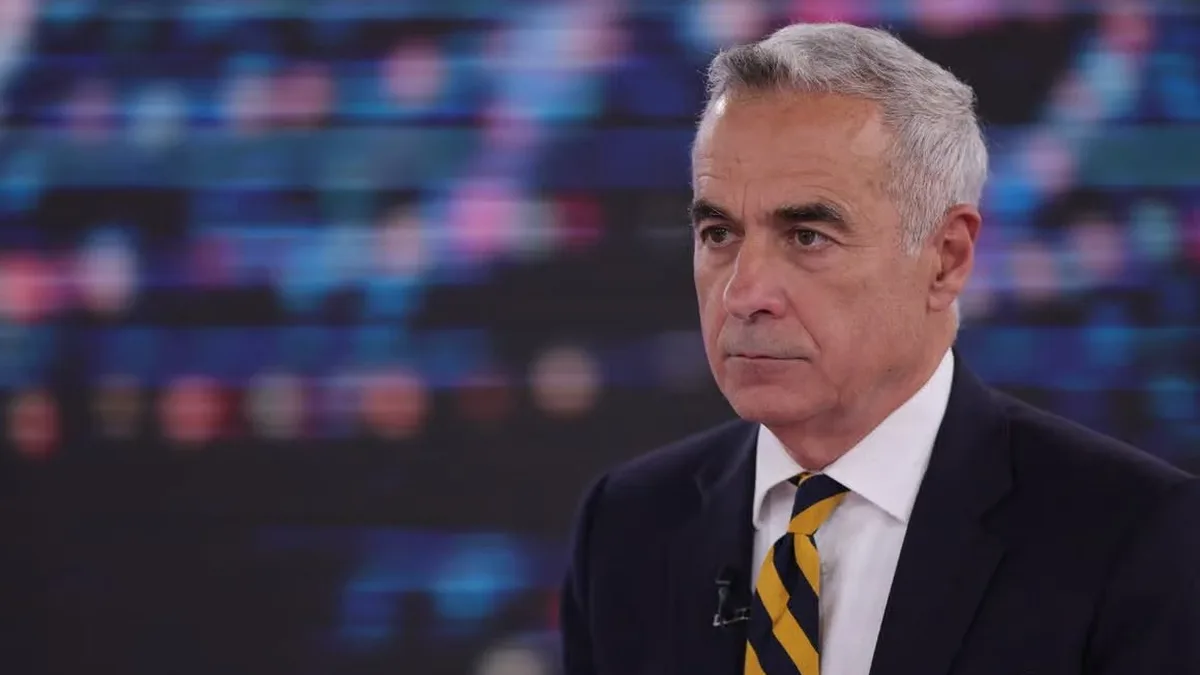 Călin Georgescu, în costum închis și cravată cu dungi galbene, într-un studio, cu microfon la rever.