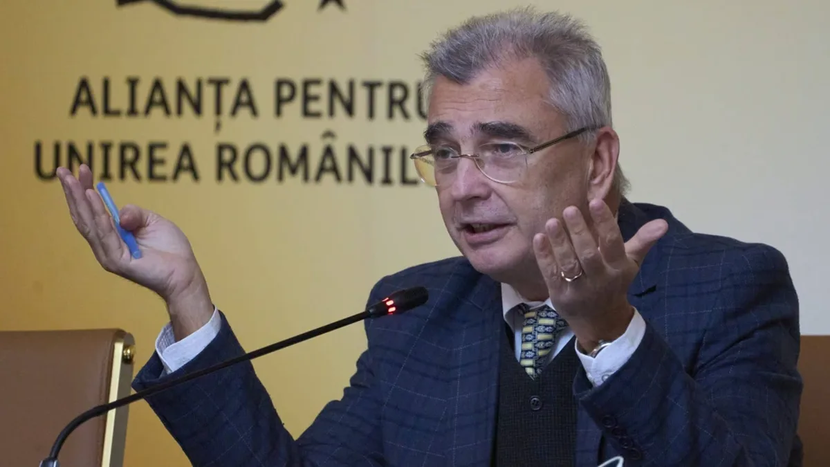 Petrișor Peiu gesticulează cu ambele mâini la microfon, în fața unui panou al Alianței pentru Unirea Românilor.