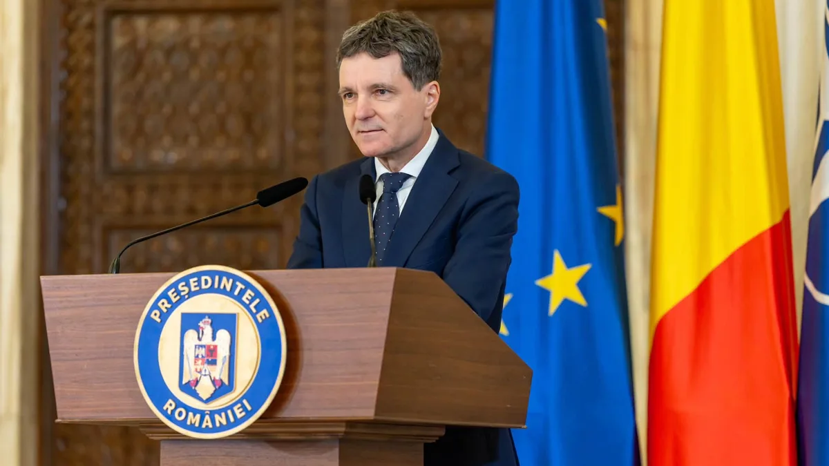 Nicușor Dan la pupitrul prezidențial, cu microfoane și drapelele României și Uniunii Europene în fundal.