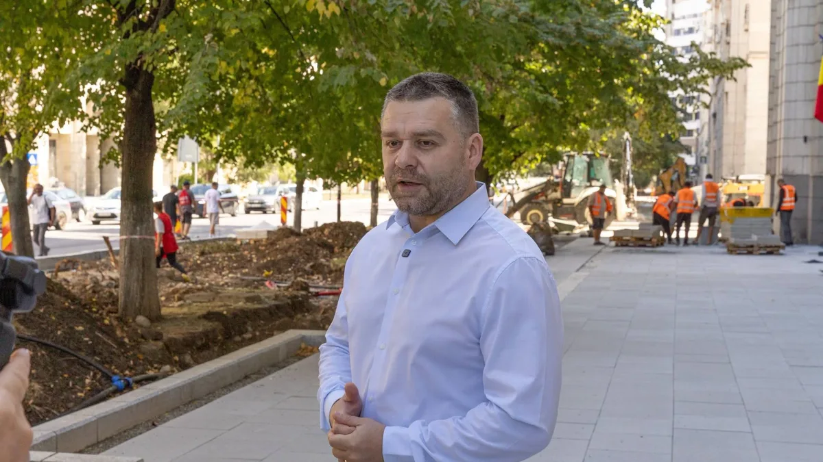 Ciprian Ciucu vorbește pe un trotuar în reamenajare, cu muncitori și un buldoexcavator în fundal.