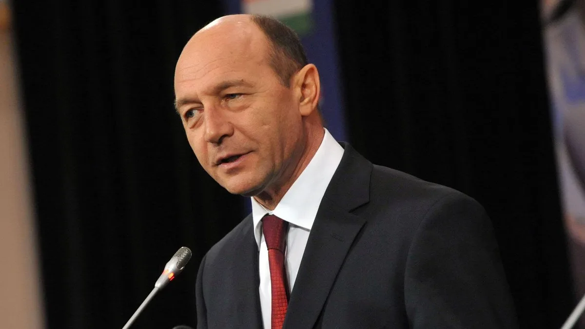 Traian Băsescu, în costum închis și cravată roșie, vorbește în fața mai multor microfoane.