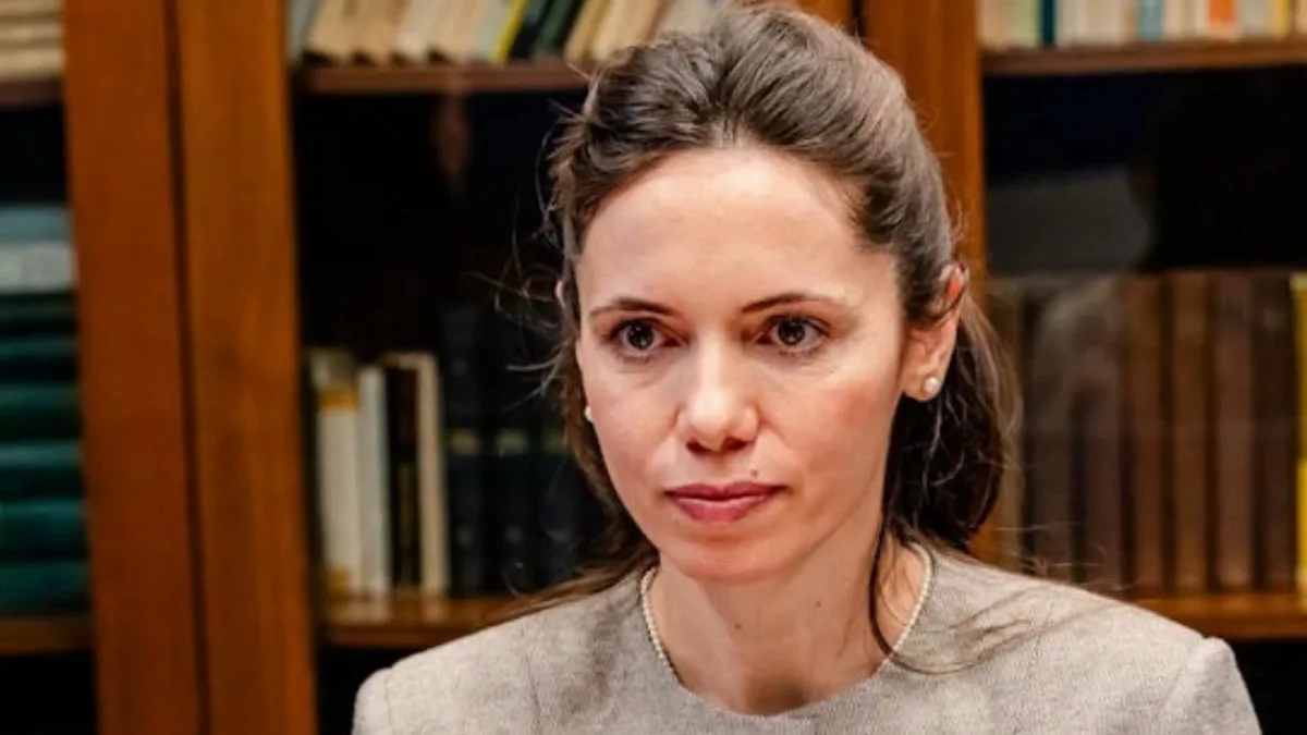 Mirabela Grădinaru, așezată la o masă cu documente, în fața unor rafturi cu cărți.