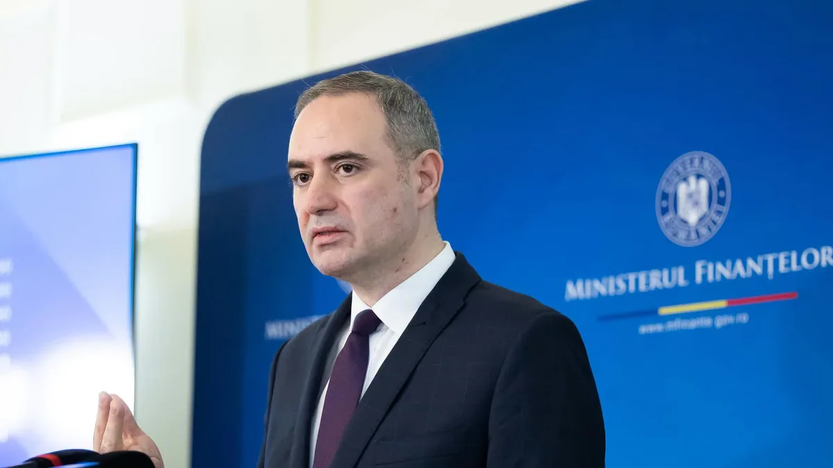 Alexandru Nazare vorbește la microfoane, în fața unui panou al Ministerului Finanțelor.