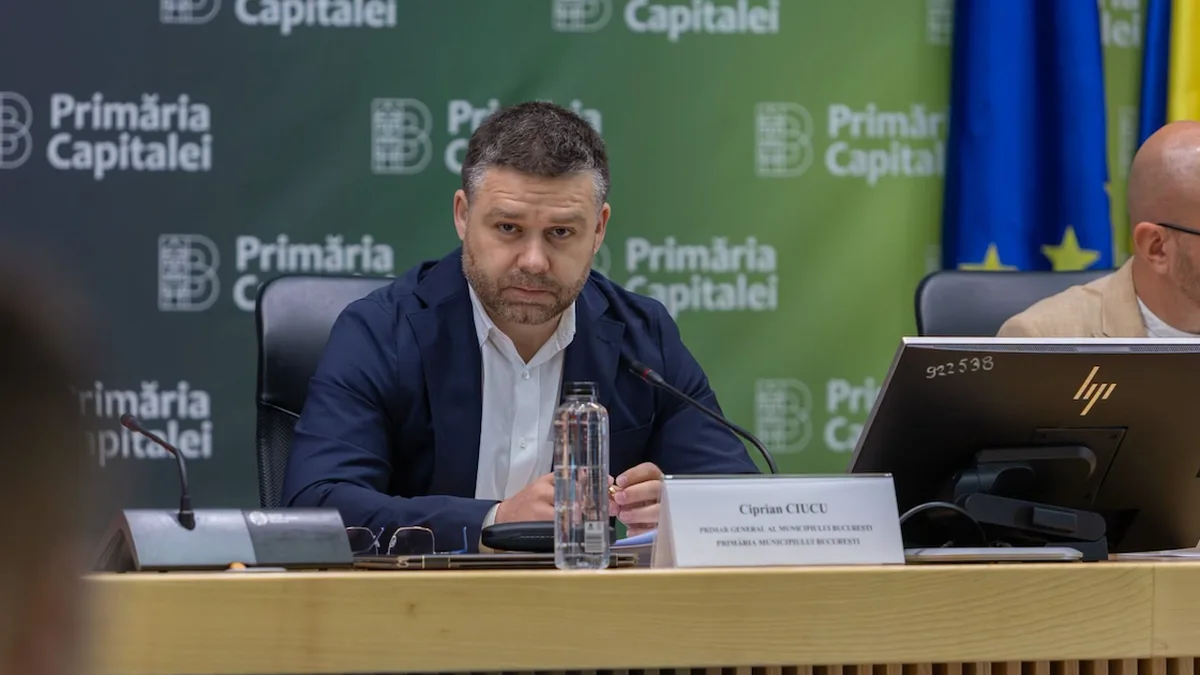 Ciprian Ciucu la o masă cu microfon și documente, în fața unui panou cu sigla Primăriei Capitalei.