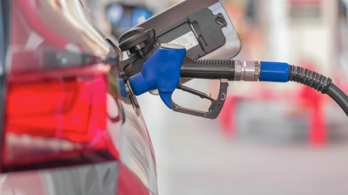 Pistol albastru de alimentare introdus în rezervorul unui autoturism, cu furtunul întins spre dreapta.