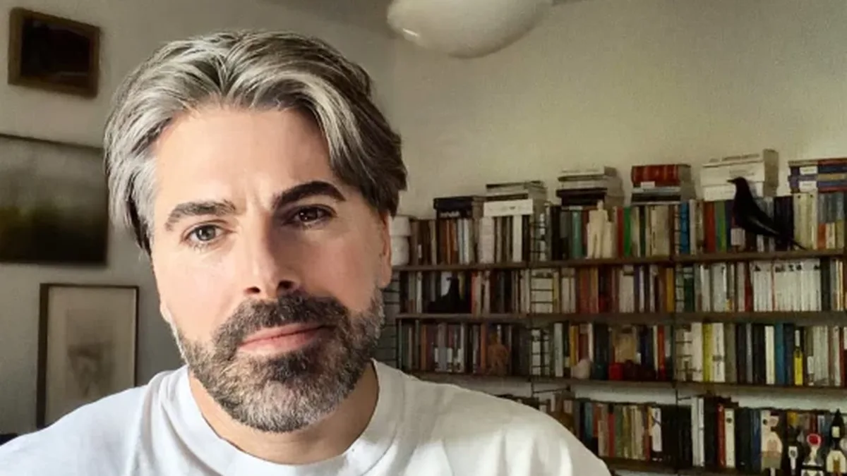 Maurice Munteanu, în tricou alb, într-o încăpere cu rafturi de cărți.