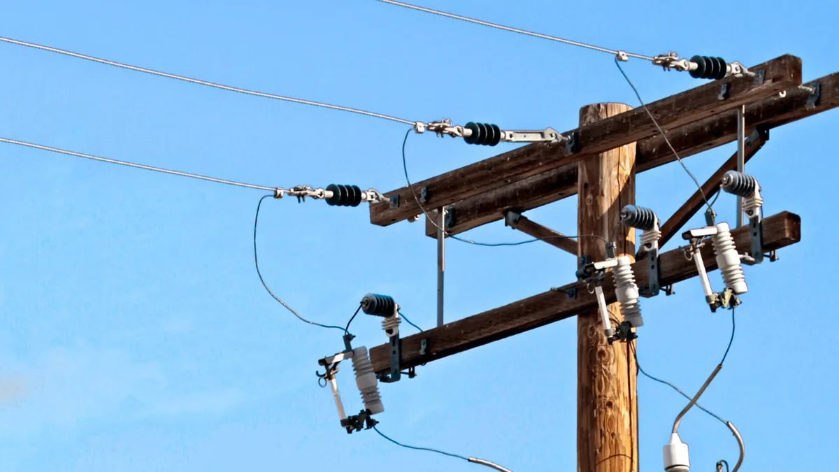 Stâlp din lemn cu conductoare electrice, izolatoare și echipamente de protecție, pe fundalul unui cer albastru.