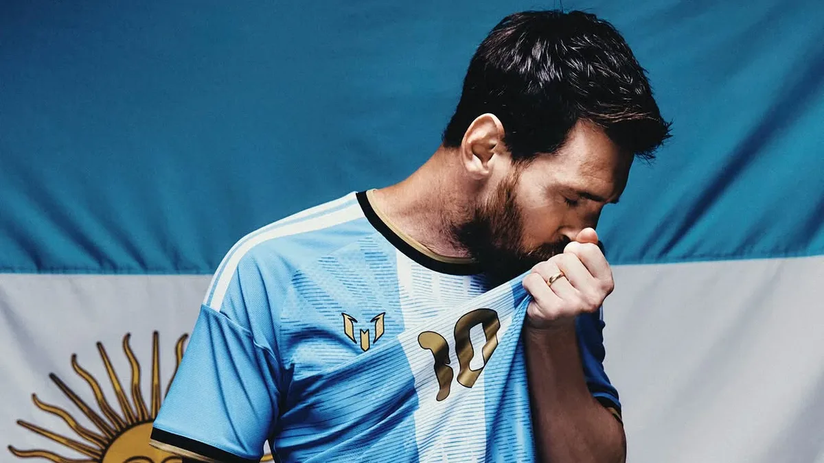Lionel Messi sărută tricoul cu numărul 10, în fața drapelului Argentinei.
