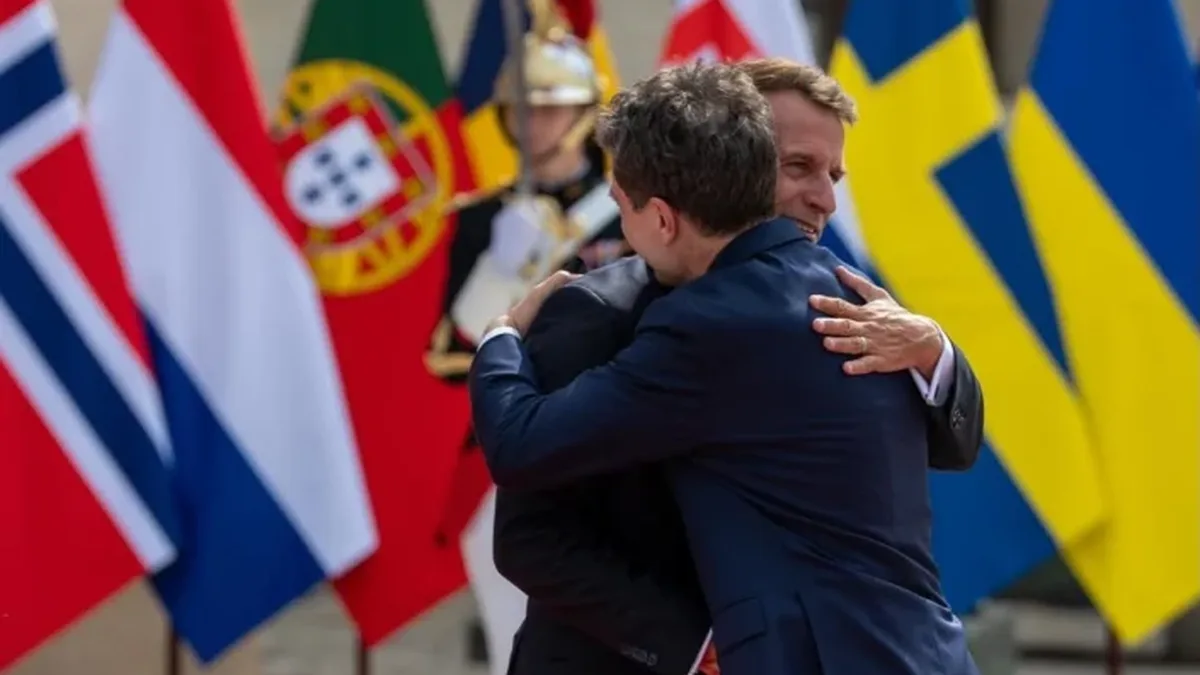 Nicușor Dan și Emmanuel Macron se îmbrățișează în fața unor drapele, cu un militar de gardă în fundal.