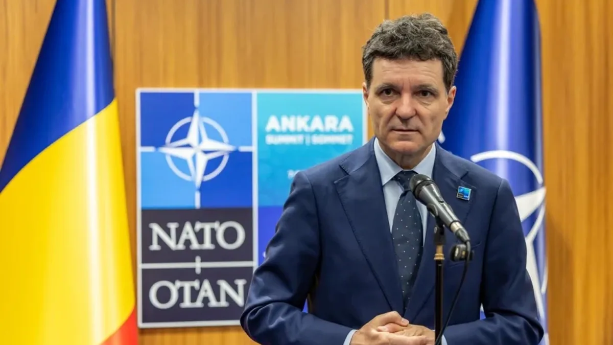 Nicușor Dan la microfon, între drapelele României și NATO, cu un panou al alianței în fundal.