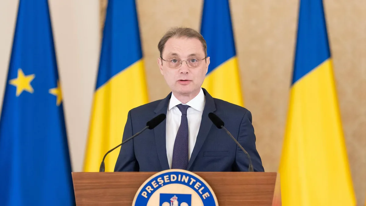 Luca Niculescu vorbește la un pupitru cu însemnele Președintelui României, între drapele românești și europene.
