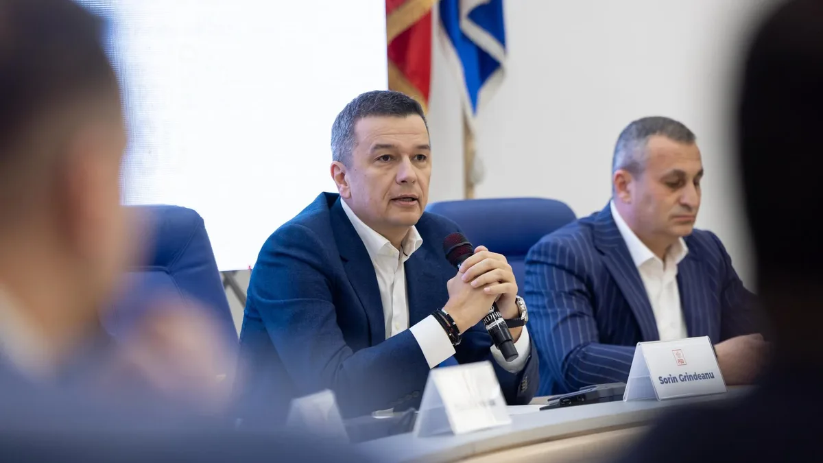 Sorin Grindeanu vorbește la microfon, așezat la o masă de reuniune, lângă un alt participant.