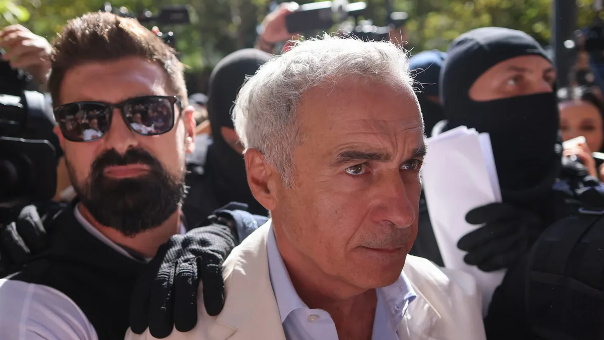 Călin Georgescu, în sacou deschis, înconjurat de persoane cu echipament tactic, în fața camerelor de presă.